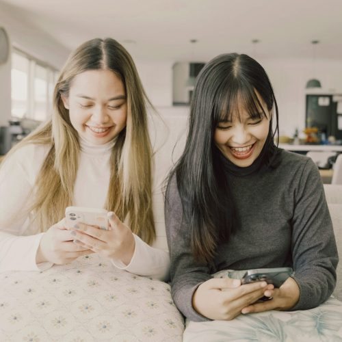 Happy Asian young adult women using phone at home